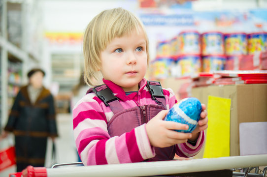 Adorable girl sit on shopping cart with christmas chocolate egg