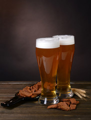 Glasses of beer with snack on table on dark background