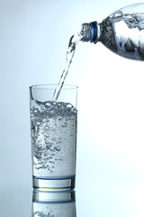 Pour water from bottle into  glass, on light blue background