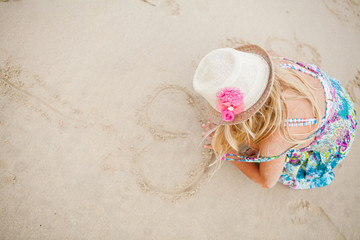 Fototapeta na wymiar Young girl drawing heart shapes in sand