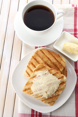 Grilled bread with butter and cup of coffee on wooden table