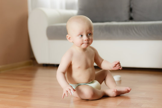 6 month infant sitting on a wooden floor wearing only a diaper