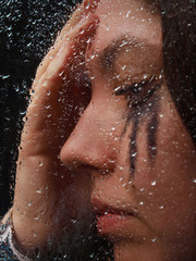 A girl is thinking standind behind the glass on one of rainy day
