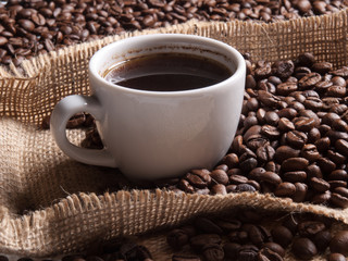 white cup with coffee on burlap background with beans