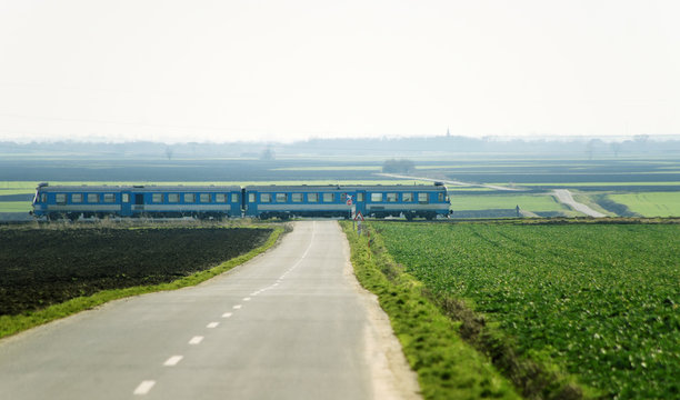 Blue train crossing over rural road