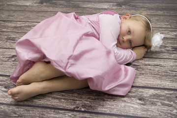 Dziewczynka w różowej sukience leżąca na podłodze - obrazy, fototapety, plakaty