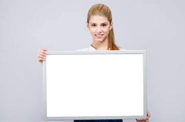 Young blonde student girl smiling holding a white blank board.