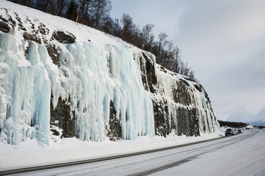 Winter road against frozen waterfall in Norway.