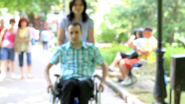 Young couple in park. Her husband is in wheelchair.