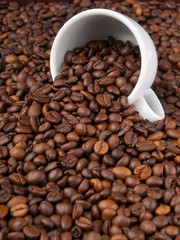 A white cup with many coffee beans on coffe background