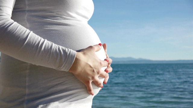 Close up pregnant woman touching belly near the sea