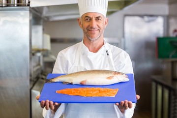 Confidence chef holding tray of raw fish in kitchen