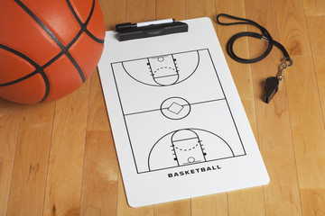 A basketball with coach's clipboard and whistle on a wooden gymn