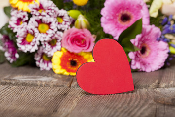 Fototapeta na wymiar Rotes Herz mit buntem Blumenstrauß im Hintergrund