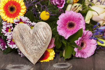 Obraz na płótnie Canvas Rustikales Holzherz vor einem Blumenstrauß auf Holztisch