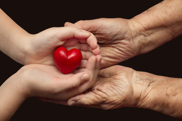 little girl and elderly woman keeping red heart in their palms t