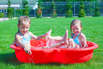 Two little sisters playing and splashing in the pool on a hot