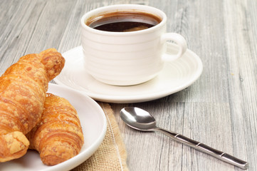 Two croissants on a plate and a cup of black coffee