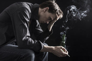 Depressed smoking man sitting on chair on black background