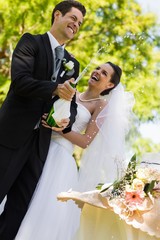 Newlywed couple with groom opening champagne bottle at park