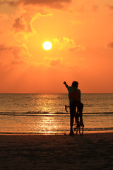 Fototapeta premium Silhouette of a biker on the beach point to sunset