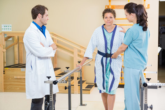 Physical Therapist With Doctor Assisting Female Patient In Walki