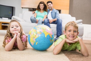 Fototapeta premium Smiling siblings lying on the rug with a globe