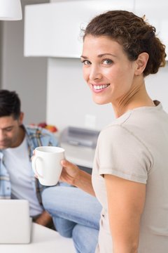 Cheerful woman drinking coffee while partners uses laptop