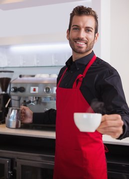 Happy young barista holding jug and cup of coffee