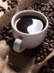 white cup with coffee on burlap background with beans