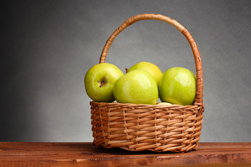 juicy green apples in basket on wooden table on gray background