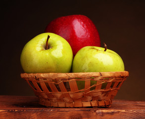 juicy sweet apples in basket on wooden table on brown