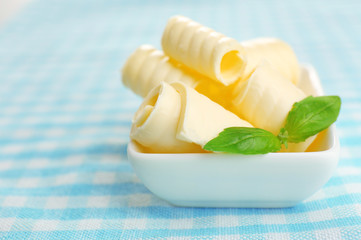 Curls of fresh butter with basil in bowl, on blue tablecloth
