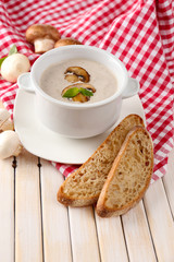 Mushroom soup in white pot, on napkin, on wooden background