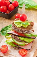 Sandwich with ham and fresh vegetables on a wooden background
