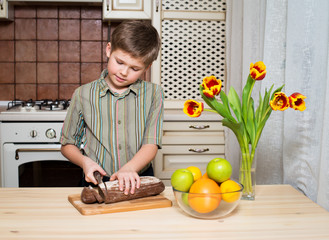 Smiling boy cutting a slice of bread. Healthy food.