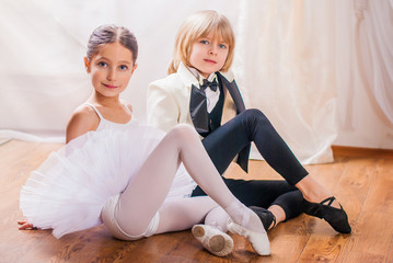 small little ballerina in a white tutu and a boy artist sit next to each other on the floor....