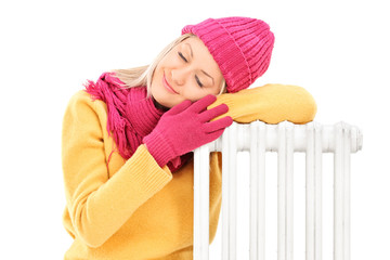 Young female in winter clothes resting on a radiator