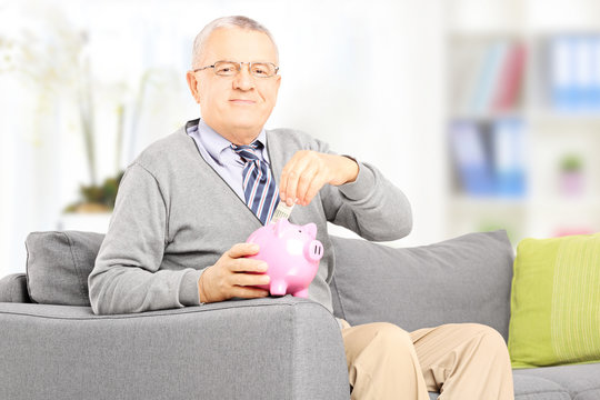 Gentleman sitting on sofa and putting money into piggybank