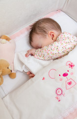 Fototapeta na wymiar Baby girl sleeping in a cot with pacifier and toy