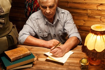Fototapeta na wymiar Senior writing letter with quill pen in homely wooden interior
