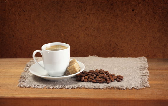 Coffee beans, cup, saucer, sugar, napkin on wooden table