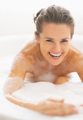 Naklejka premium Smiling young woman playing with foam in bathtub