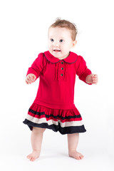 Sweet baby girl in a red dress making her first steps