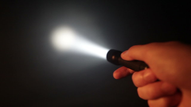 Hand with pocket flashlight looking for something in darkness