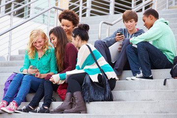 High School Students Sitting Outside Building With Phones