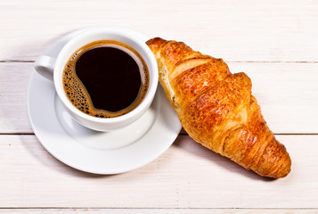 Coffee cup with a croissant isolated on wooden table 