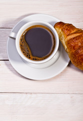 Coffee cup with a croissant isolated on wooden table 
