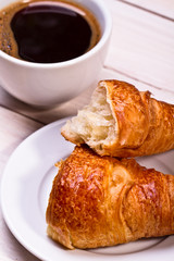 Coffee cup with a croissant isolated on wooden table 