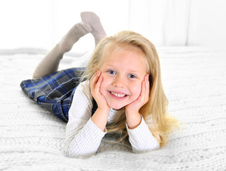 Adorable blonde blue eyed little girl lying happy on bed